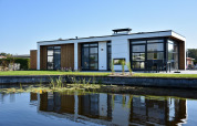 Lodge moderno con ventanales y detalles de madera, reflejado en un estanque bajo un cielo despejado.