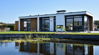 Moderne lodge met grote ramen en houten details, weerspiegeld in een vijver onder een heldere lucht.