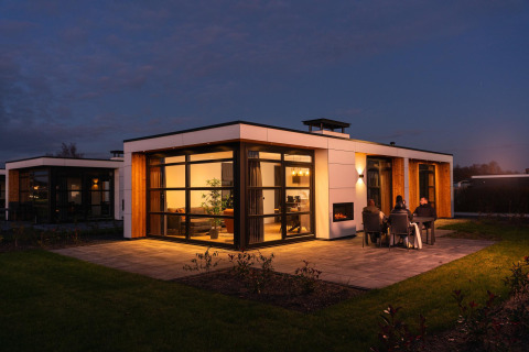 Abendaufnahme der Villa Nautica Lodge mit beleuchteten Fenstern und Gästen, die draußen auf der Terrasse sitzen.