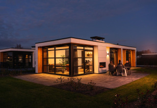Vista nocturna de la Villa Nautica con ventanas iluminadas y visitantes sentados en la terraza exterior.