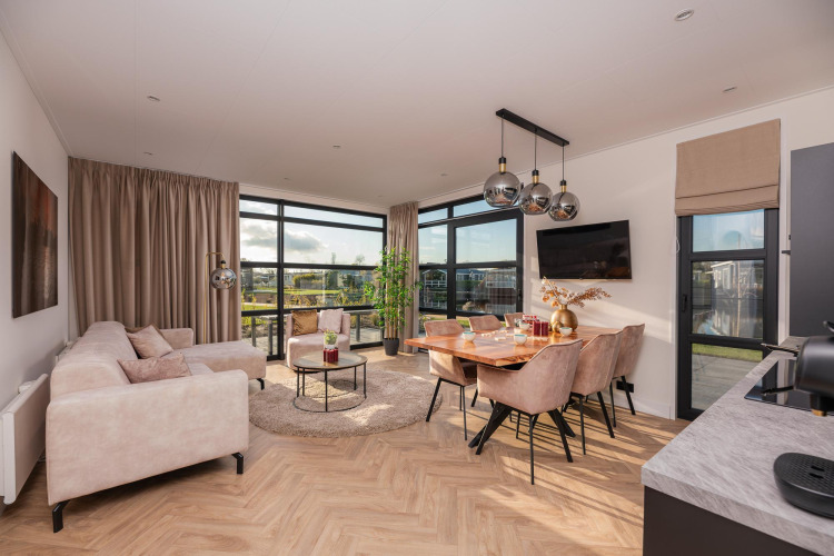 Helles, modernes Wohnzimmer einer Lodge mit großen Fenstern, Essbereich und bequemen Sofas.