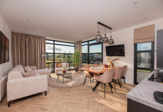 Helles, modernes Wohnzimmer einer Lodge mit großen Fenstern, Essbereich und bequemen Sofas.