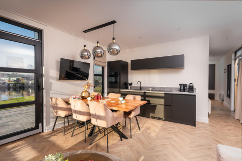 Cocina y comedor modernos en una cabaña, con ventanales grandes y vistas al lago en el exterior.