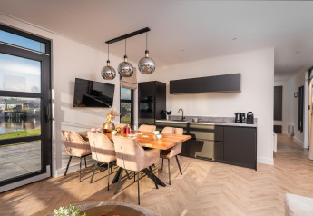 Moderne lodge med åbent køkken, spisebord og store vinduer, der tilbyder udsigt til søen udenfor.