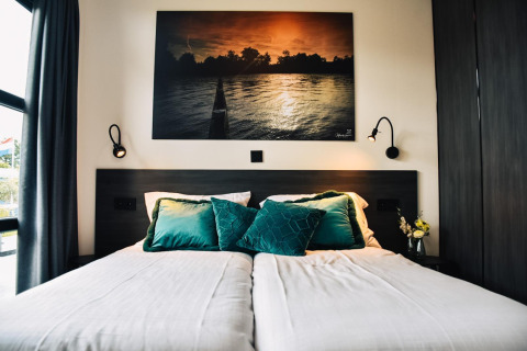 Modernes Bett mit grünen Kissen und Wandkunst in der Villa Nautica, MarinaPark Residentie Nieuw Loosdrecht, Niederlande.