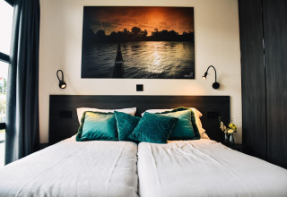 Modernes Bett mit grünen Kissen und Wandkunst in der Villa Nautica, MarinaPark Residentie Nieuw Loosdrecht, Niederlande.