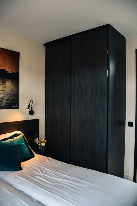 Modernes Schlafzimmer mit dunklem Kleiderschrank und gemütlichem Bett in der Villa Nautica, MarinaPark Residentie Nieuw Loosdrecht.