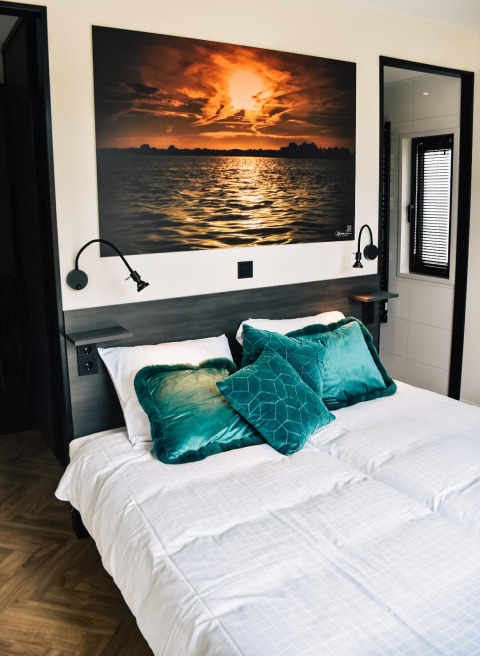 Dormitorio en Villa Nautica en MarinaPark Residentie Nieuw Loosdrecht con cama doble y cuadro de un atardecer.