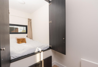 Acogedora habitación con ropa de cama blanca y armarios abiertos en Villa Nautica, MarinaPark Nieuw Loosdrecht.