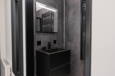 Baño moderno en una cabaña, con lavabo oscuro, espejo grande, grifería negra y paredes grises.