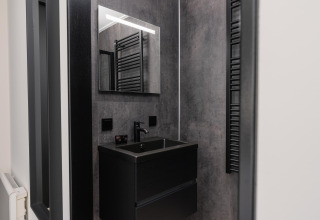 Baño moderno en una cabaña, con lavabo oscuro, espejo grande, grifería negra y paredes grises.