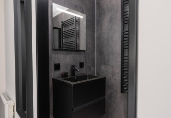 Moderne lodgebadkamer met donkere wasbak, grote spiegel, zwarte kranen en grijze wandafwerking.