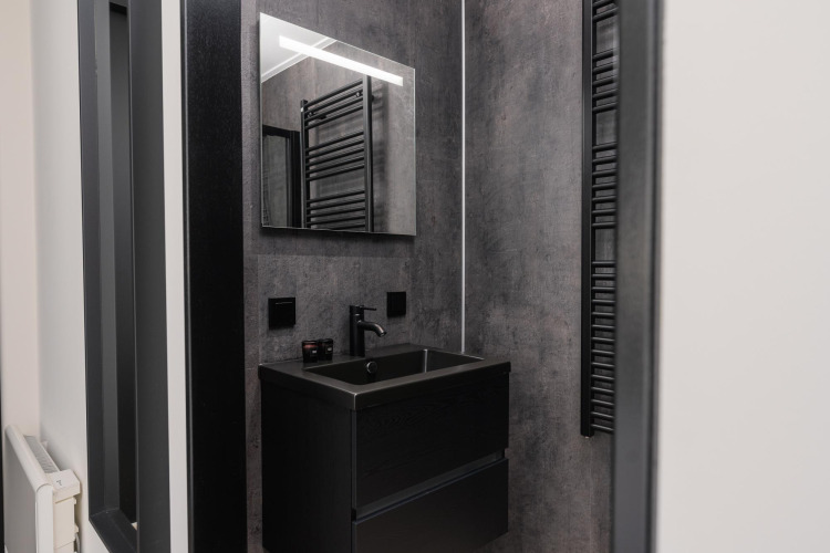 Salle de bain moderne dans un lodge avec lavabo noir, grand miroir, robinet noir et murs gris.