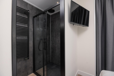 Baño moderno de lodge con cabina de ducha negra, radiador toallero y televisor en la pared.