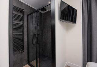 Baño moderno de lodge con cabina de ducha negra, radiador toallero y televisor en la pared.