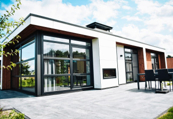 Moderne lodge met grote ramen en buitenterras, omgeven door natuur en deels bewolkte lucht.