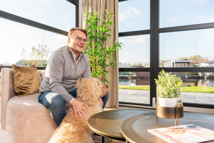 Mann sitzt mit Hund im Wohnzimmer der Villa Nautica, MarinaPark Residentie Nieuw Loosdrecht, Niederlande.