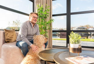 Man zit met zijn hond in het salon van Villa Nautica, MarinaPark Residentie Nieuw Loosdrecht, Nederland.