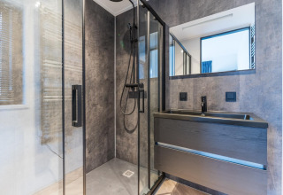 Baño moderno con ducha de vidrio, lavabo oscuro y espejo en Villa Nautica, MarinaPark Residentie Nieuw Loosdrecht.