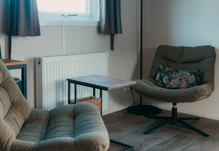 Zona de salón acogedora con sillones, mesa y cojín floral en Veluwe lounge + sauna de De Boshoek, Países Bajos.