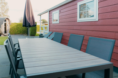 Buitenlounge met tafel en stoelen bij een rode lodge en sauna in vakantiepark De Boshoek, Nederland.