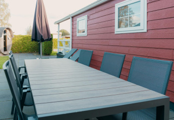 Zona soggiorno all’aperto con tavolo e sedie presso lodge rosso e sauna a Holiday park De Boshoek, Paesi Bassi.