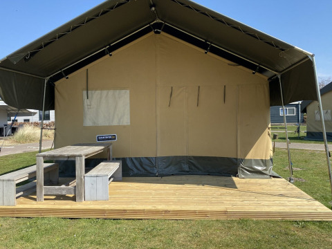 Safaritent met houten terras en banken bij Holiday Park Duinhoeve in Nederland op een zonnige dag.