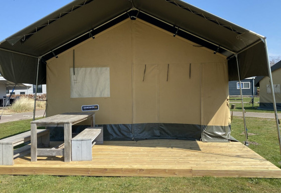 Safaritent met houten terras en banken bij Holiday Park Duinhoeve in Nederland op een zonnige dag.
