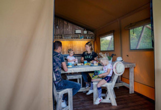 En familie nyder et måltid sammen i en hyggelig Glampinglodge GL i Holiday Park BreeBronne, Holland.