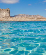 Agua cristalina y una antigua torre de piedra junto a la costa en Candemil, norte de Portugal, bajo el sol.