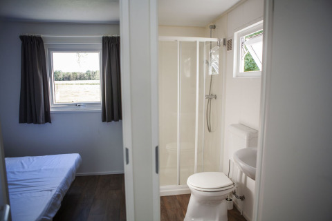 Interior de la Veluwelodge en el parque vacacional De Boshoek, mostrando dormitorio y baño privado con ducha.