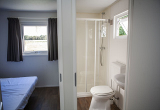 Interior de la Veluwelodge en el parque vacacional De Boshoek, mostrando dormitorio y baño privado con ducha.
