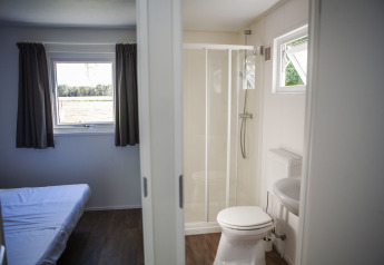 Indvendig udsigt fra Veluwelodge på De Boshoek, viser et soveværelse og privat badeværelse med bruser.