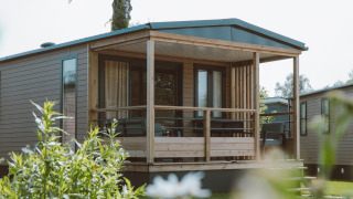 Tiny Lodge tiny house bij Holiday park De Boshoek in Nederland met overdekte veranda en tuinzicht.