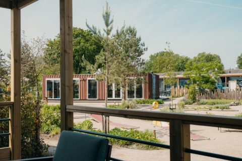 Vista desde una cabaña glamping hacia una terraza, áreas verdes, minigolf y edificios modernos tipo contenedor.