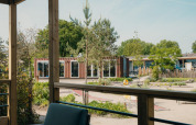 Vista desde una cabaña glamping hacia una terraza, áreas verdes, minigolf y edificios modernos tipo contenedor.