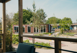 Vista desde una cabaña glamping hacia una terraza, áreas verdes, minigolf y edificios modernos tipo contenedor.