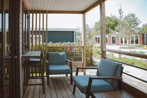 Veranda coperta di un alloggio glamping con poltrone moderne e vista sulla natura circostante.