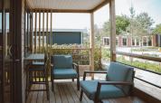 Hyggelig overdækket terrasse ved glamping, med moderne stole og bord, omgivet af grøn natur.