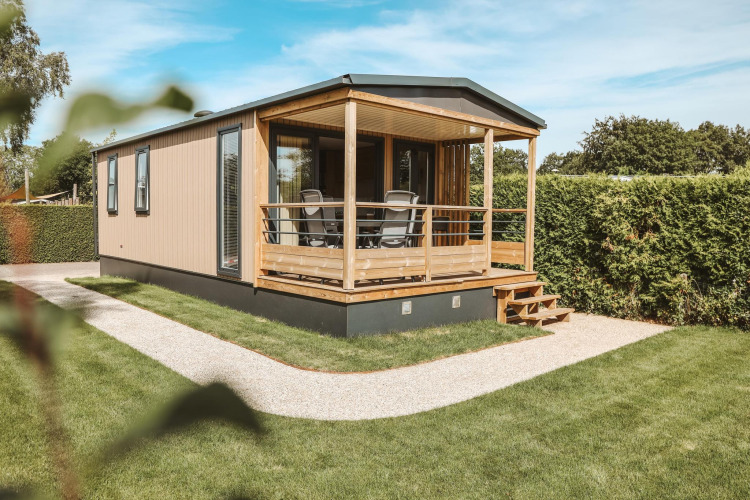 Tiny Lodge tiny house op vakantiepark De Boshoek in Nederland met veranda en groene tuin.
