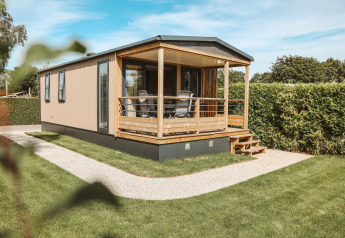 Tiny Lodge tiny house op vakantiepark De Boshoek in Nederland met veranda en groene tuin.