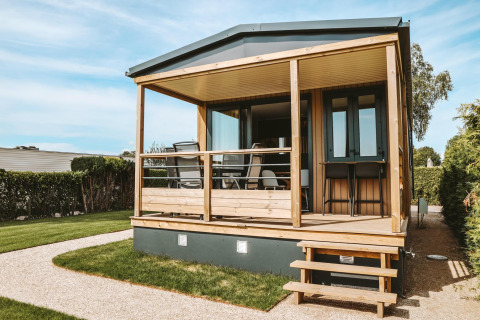 Kleines Tiny Lodge Haus mit überdachter Holzveranda im Ferienpark De Boshoek, Niederlande, sonniger Tag.