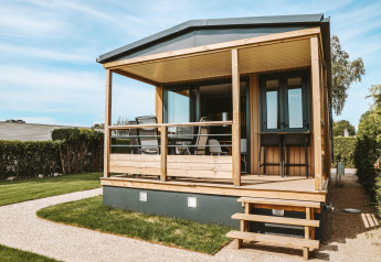Et hyggeligt Tiny Lodge lille hus med en træterrasse i Holiday park De Boshoek, Holland, på en solskinsdag.