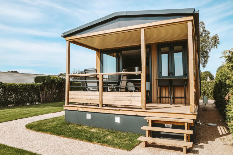 Tiny Lodge tiny house with wooden porch at Holiday park De Boshoek in the Netherlands on a sunny day.