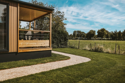 Tiny Lodge in Holiday park De Boshoek in Nederland, met terras, grasveld en zicht op een weide.