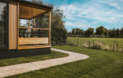 Tiny Lodge presso Holiday park De Boshoek nei Paesi Bassi, portico, prato e vista su un campo aperto.