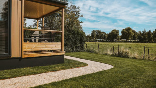 Tiny Lodge på Holiday park De Boshoek, Nederlandene, med veranda, græsplæne og udsigt til mark.