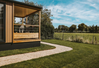 Tiny Lodge im Holiday Park De Boshoek, Niederlande, mit Veranda, Rasen und Blick auf Felder.