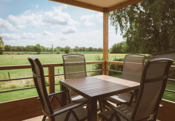 Terrasse med fire havestole og bord på Tiny Lodge, De Boshoek feriepark, Holland, udsigt over marker.