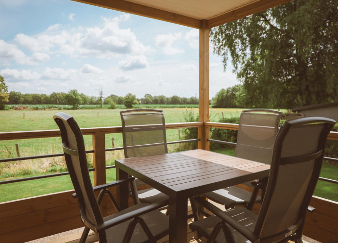 Terras met vier stoelen en tafel bij Tiny Lodge, Holiday park De Boshoek, Nederland, uitzicht op weiland.